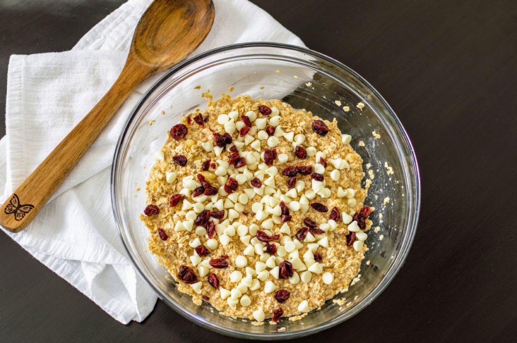 Oatmeal cranberry muffin batter in a glass bowl with a wooden spoon.