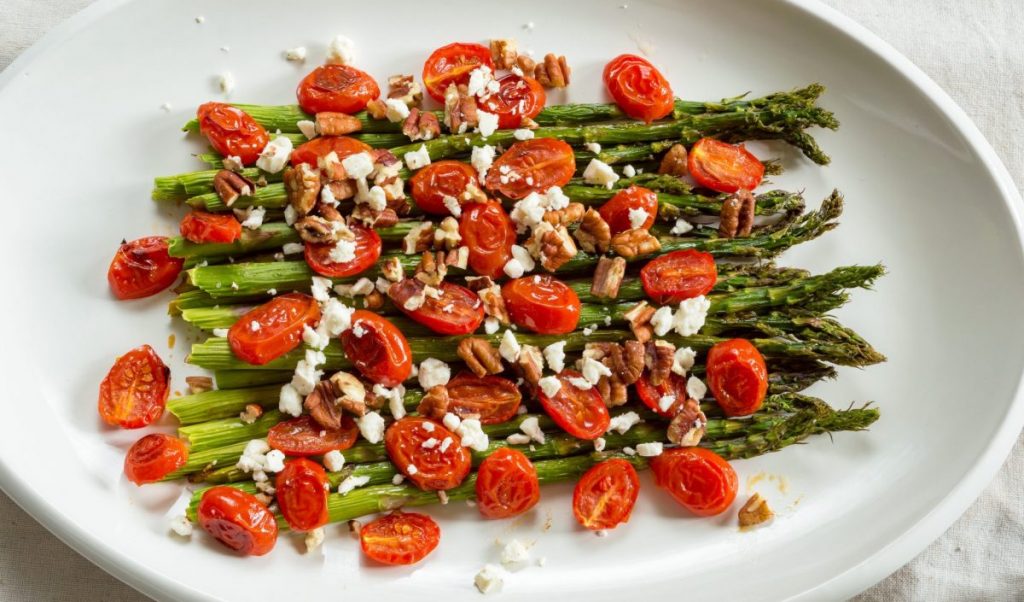 Asparagus, tomatoes, pecans, and feta cheese on a white plate.