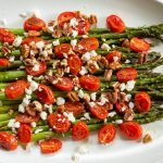 Asparagus, tomatoes, pecans, and feta cheese on a white plate.