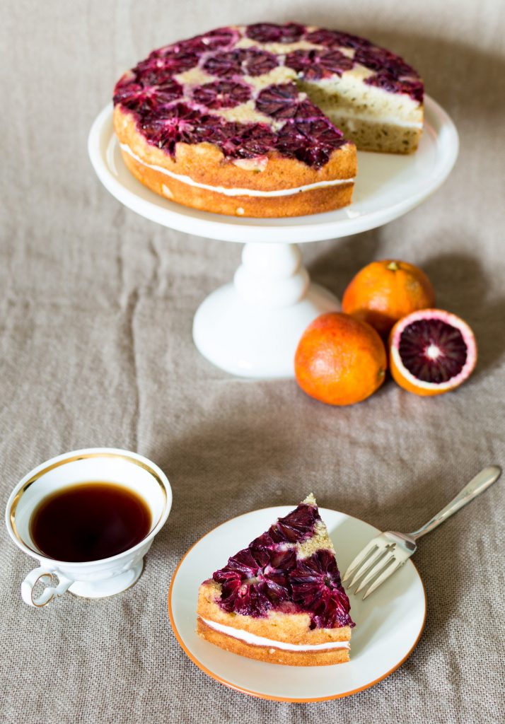 blood orange spice cake on white cake stand with tea and oranges