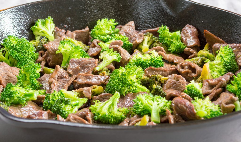 Broccoli and beef cooking in a cast iron skillet.