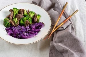 broccoli and beef in a bowl with cabbage and chop sticks