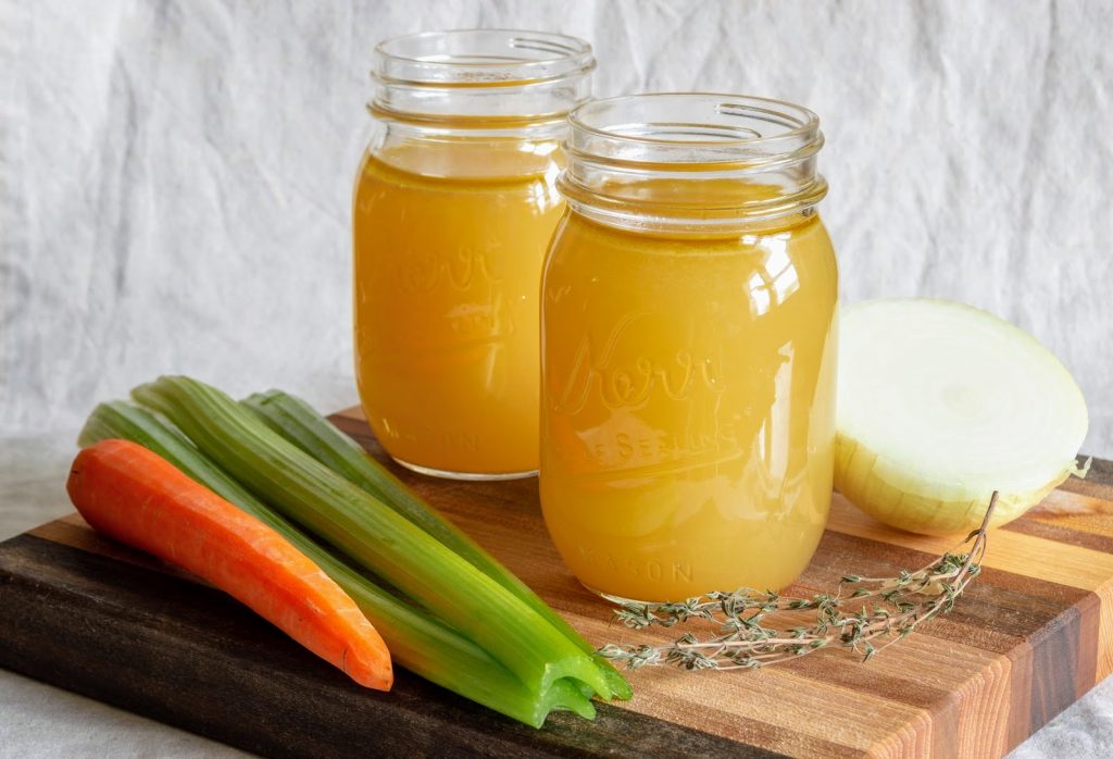stock in glass jar sitting on wooden cutting board with vegetables