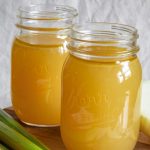 chicken stock in a glass jar sitting on a wooden cutting board
