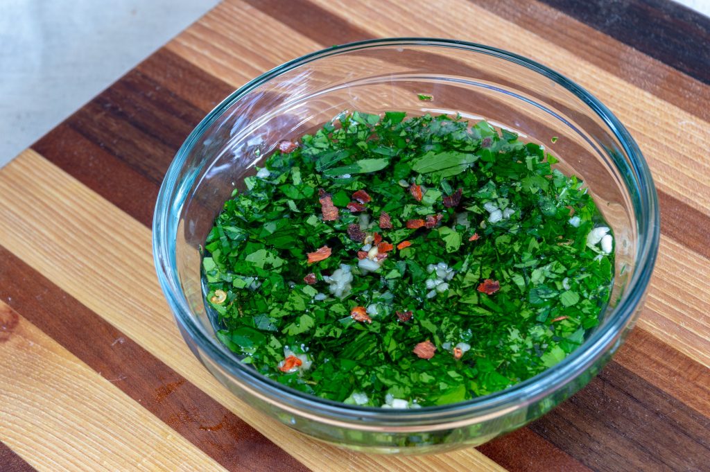 glass bowl of chimichurri on a wooden cutting board