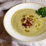 zucchini soup garnished with parsley, oil, and pecans.