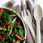 Asparagus and red pepper salad in a white salad bowl with a gray napkin and white utensils.