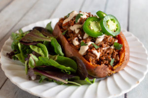 Sloppy joe baked potato with chipotle sauce, jalapenos, and salad on a white plate.