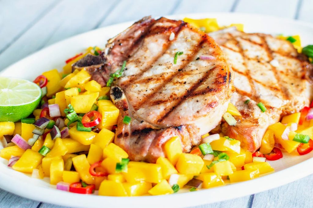Pork chop with grill marks on top of white plate with mango salsa.