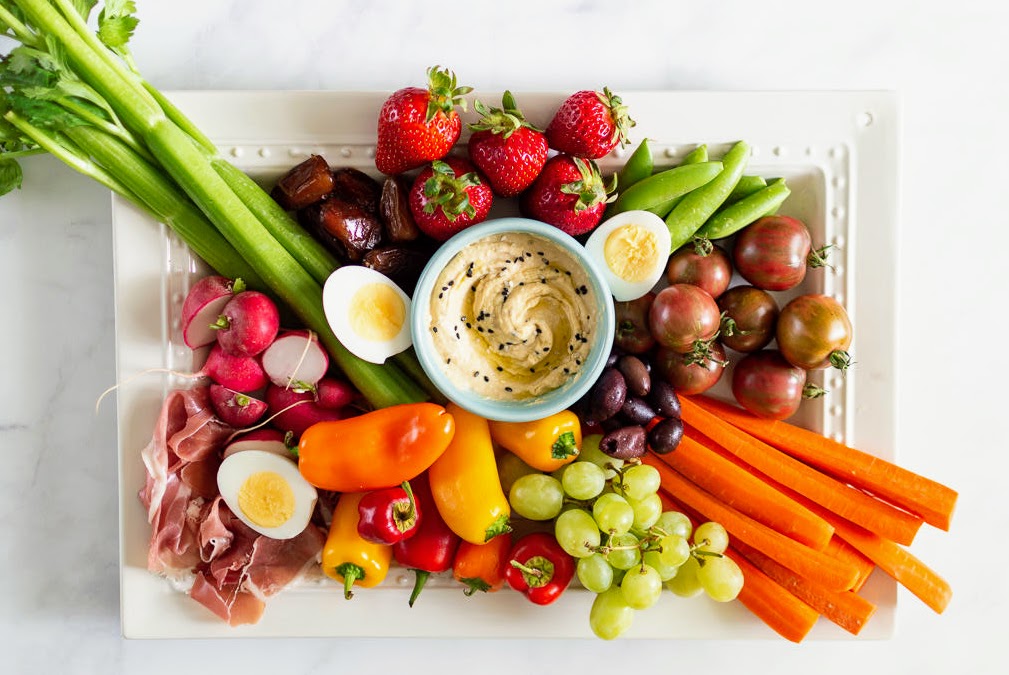 Paleo vegetable platter with peppers, carrots, celery, tomatoes, grapes, strawberries on a white platter.