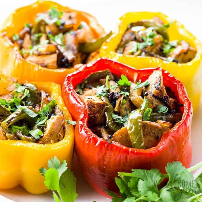Red and yellow bell peppers stuffed with chicken fajita mixture and garnished with cilantro sitting on a white plate.